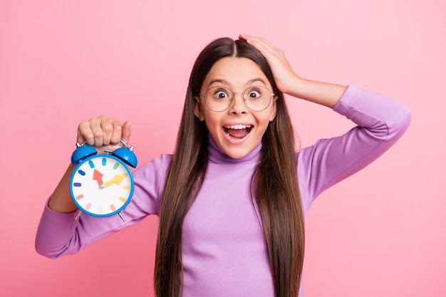 Foto von erstauntem kleinen Kind halten Uhr-Touch-Handkopf isoliert über pastellfarbenem Hintergrund