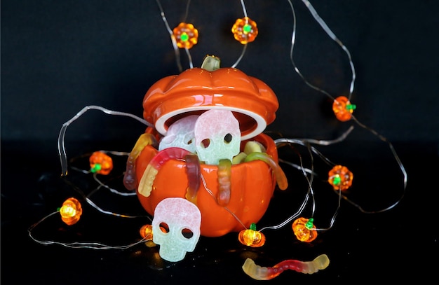 Foto foto von halloween dekorationen süßigkeiten schüssel kürbis mit süßigkeiten und führte kürbis girlande auf schwarzem rücken