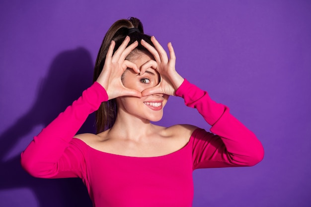 Foto von hübschen Damenfingern, die um die Augenherzform gekreuzt sind, tragen rosa unbekleidete Schultern oben isolierter violetter Farbhintergrund