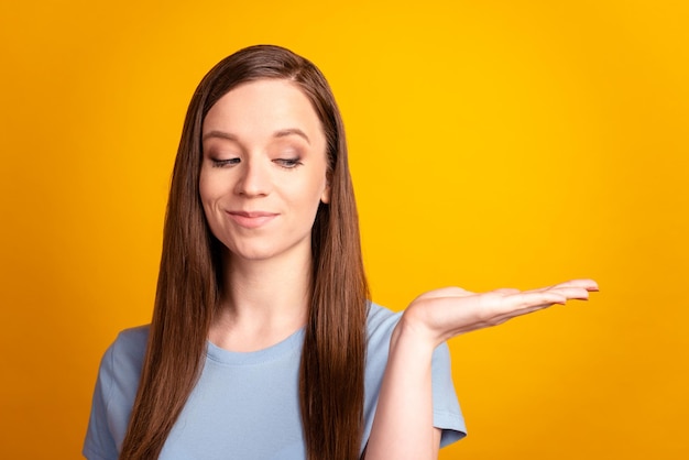 Foto von jungen attraktiven Mädchen halten Hand Promotion-Produktanzeigen zeigen Rabatt isoliert auf gelbem Farbhintergrund