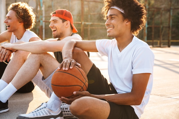 Foto foto von jungen professionellen basketballspielern, die am spielplatz im freien sitzen und spiel während des sonnigen sommertages beobachten