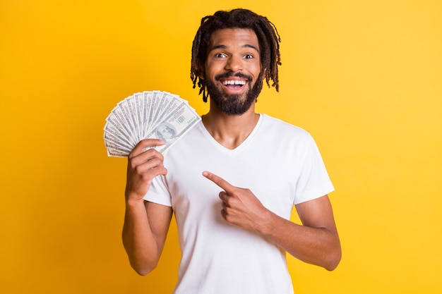 Foto von jungen schwarzen bärtigen Kerl Dreadlocks halten Finger Einkommen Cash Fan tragen weißes T-Shirt isoliert gelber Farbe Hintergrund