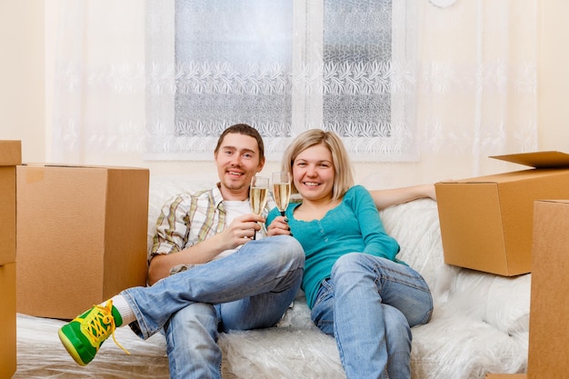 Foto von Mann und Frau mit Weingläsern mit Wein, die auf dem Sofa zwischen Kartons sitzen