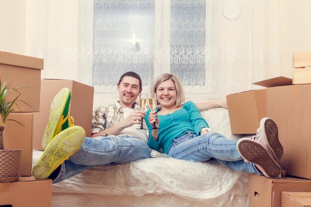 Foto von Mann und Frau mit Weingläsern mit Wein, die auf dem Sofa zwischen Kartons sitzen