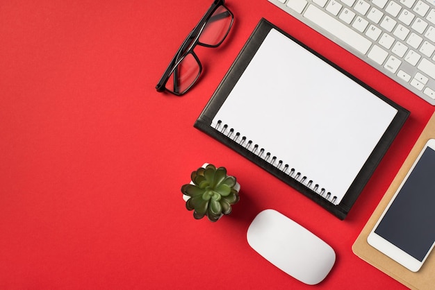 Foto von oben mit weißer Tastatur, Maus, Blumentopf, Brille, Handy und zwei Erinnerungen auf isoliertem, leuchtend rotem Hintergrund mit Leerzeichen