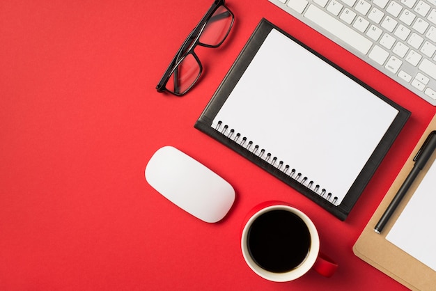 Foto von oben mit weißer Tastatur, Maus, Brille, Stift, Tasse Kaffee und zwei Erinnerungen auf isoliertem, leuchtend rotem Hintergrund mit Leerzeichen