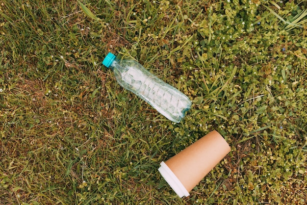 Foto von Plastikflasche und Papierkaffeetasse auf grünem Gras