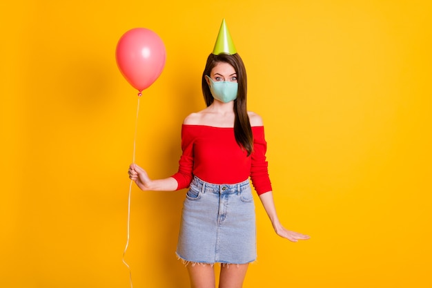 Foto von positivem Mädchen in medizinischer Maske genießen Sie eine Covid-Quarantäne-Jubiläumsparty, halten Sie Ballons tragen rote Denim-Jeans mit kurzem Minirock-Kegel einzeln auf hell glänzendem Hintergrund