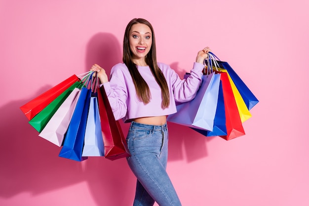 Foto von positiven fröhlichen Mädchen genießen Sie den Einkauf außerhalb des Verkaufs. Viele Taschen tragen einen stilvollen, trendigen Pullover im lila Stil einzeln auf pastellfarbenem Hintergrund