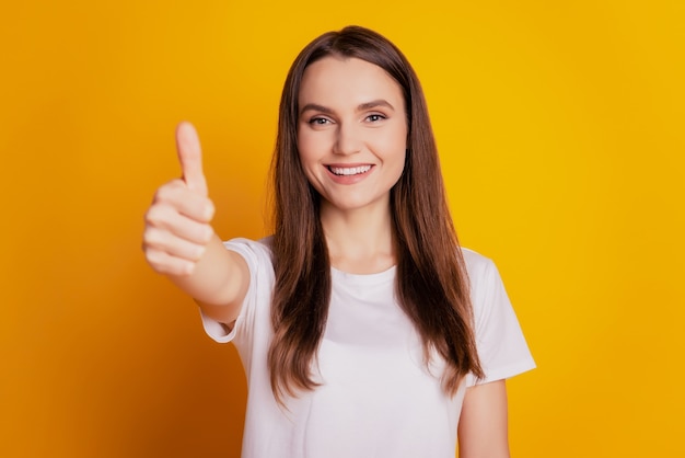 Foto von positiver Promoter-Dame zeigen Daumen hoch tragen weißes T-Shirt, das auf gelbem Hintergrund posiert