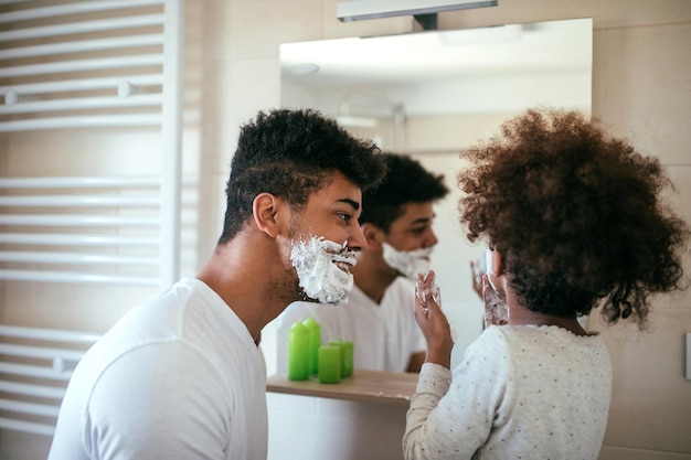 Foto von schwarzem Vater und Tochter, die sich im Badezimmer mit Rasierschaum amüsieren