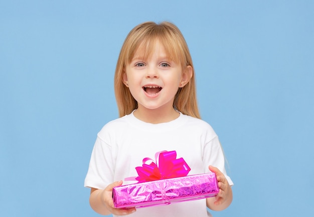 Foto von süßen süßen Schulmädchen trägt weißes T-Shirt lächelnd mit gelber und grüner Geschenkbox isoliert blauer Hintergrund