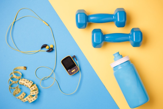 Foto von Themen der Fitness. Spieler, Hanteln, Flasche Wasser, Zentimeterband auf blauem und gelbem Hintergrund