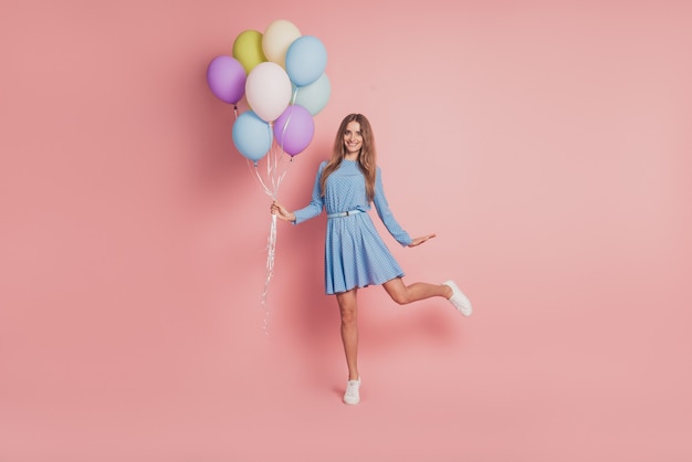 Foto von verspieltem Mädchen mit bunten Luftballons in kurzen Rockschuhen auf rosa Hintergrund