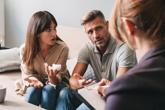 Foto von verwirrtem unglücklichen Paar Mann und Frau, die sich mit einem Psychologen über eine Therapiesitzung im Zimmer unterhalten