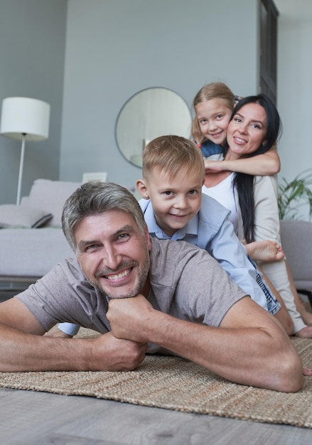 Foto von vier Mitgliedern der Adoptivfamilie, die auf dem Boden liegen, toothy, lächelnd, flauschiger Teppich, gemütliche Apartments