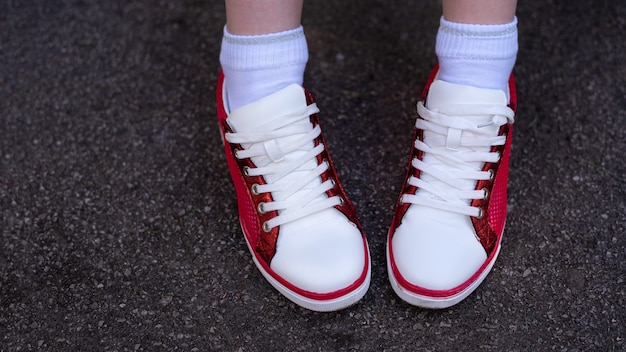 Foto von weiblichen Beinen in roten und weißen Turnschuhen auf grauem nassem Asphalt