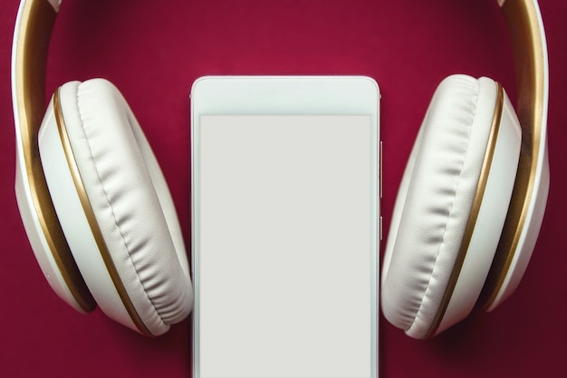 Foto von weißen Kopfhörern und Smartfone für Musik auf rotem Hintergrund. Attrappe, Lehrmodell, Simulation.