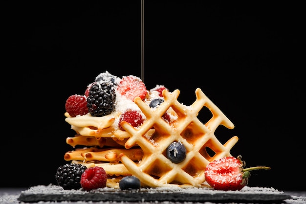 Foto von Wiener Waffeln mit Himbeeren, Erdbeeren mit Puderzucker bestreut, mit Honig auf schwarzem leerem Hintergrund im Studio