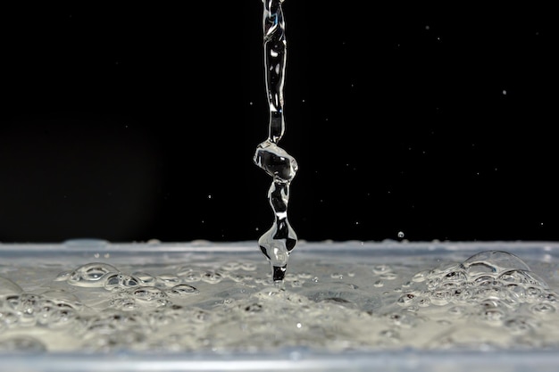 Foto von wunderschönen Wassertropfen, die auf Wasser fallen und auf schwarzem Hintergrund spritzen