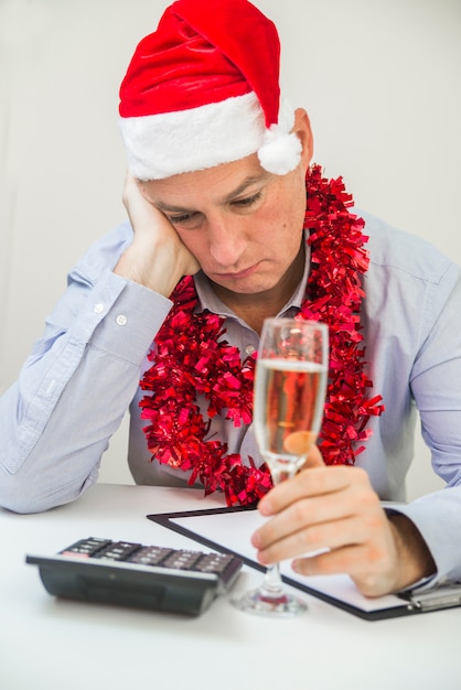 Foto von Young Depressed Geschäftsmann Sitzung Im Büro. Business-Mann feiern Frohe Weihnachten und Happy New Year tragen Santa Hut