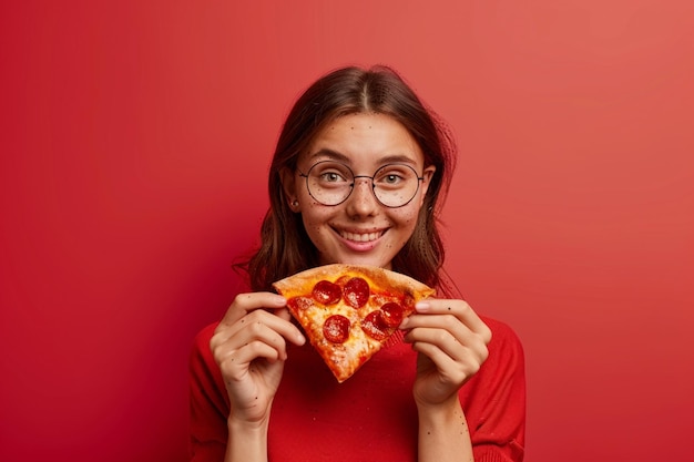 Foto von zufrieden hält ein Stück Pizza sieht glücklich direkt trägt stilvolle Casual Outfit