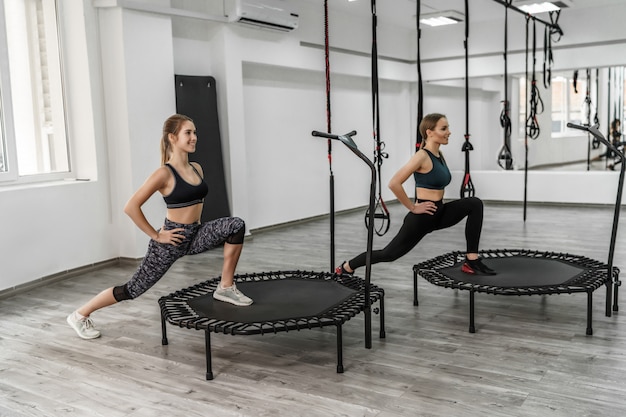 Foto von zwei aktiven Mädchen und Fitnesstrainer in Sportkleidung, die Übungen zum Dehnen machen