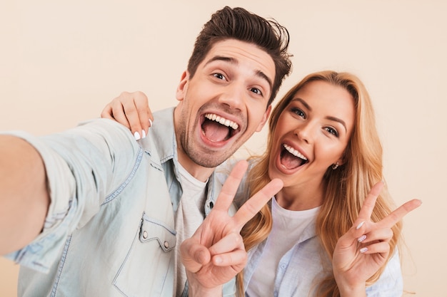 Foto von zwei glücklichen Menschen Mann und Frau umarmen und Selfie Foto machen, während Friedenszeichen mit Lächeln zeigen