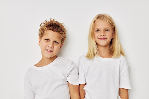 Foto von zwei Kindern in weißen T-Shirts stehen neben beigem Hintergrund