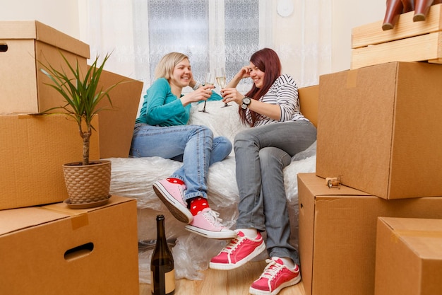 Foto von zwei Mädchen, die zwischen Kartons auf dem Sofa sitzen