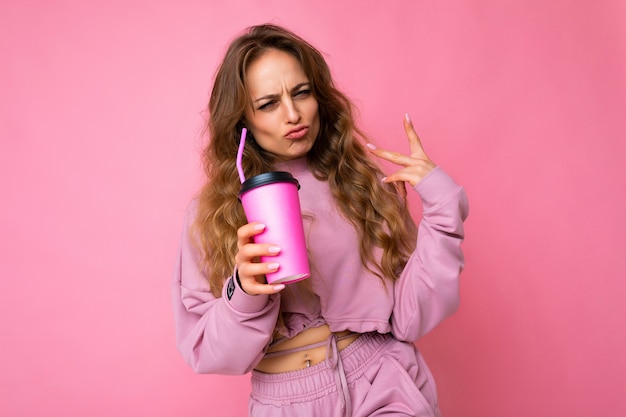 Fotoaufnahme der schönen jungen positiven freudigen blonden Frau, die rosa Sportkleidung lokalisiert trägt