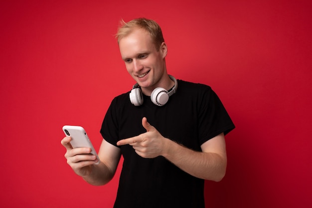 Fotoaufnahme des schönen positiven gut aussehenden jungen Mannes, der lässiges stilvolles Outfit trägt