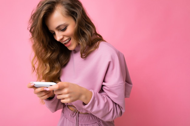 Fotoaufnahme einer attraktiven, gut aussehenden jungen frau, die ein lässiges, stylisches outfit trägt, das auf dem hintergrund isoliert ist, mit leerem raum in der hand und mit handy-messaging-sms angeschaut