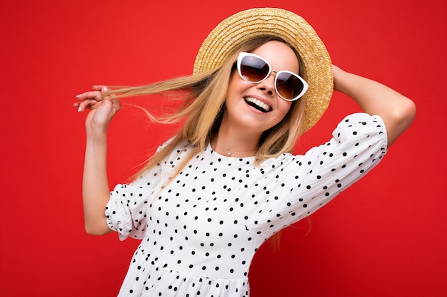 Fotoaufnahme einer schönen positiven jungen blonden Frau, die sommerliche Freizeitkleidung und eine stilvolle Sonnenbrille trägt, die auf buntem Hintergrund isoliert ist und zur Seite schaut