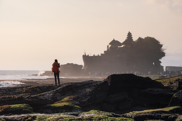 Fotograf, der auf Küste mit Tanah-Lot-Tempelhintergrund steht