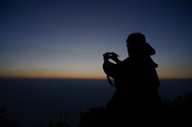 Fotograf, der Fotos auf Bergblick mit Schattenbildsonnenaufgang macht.