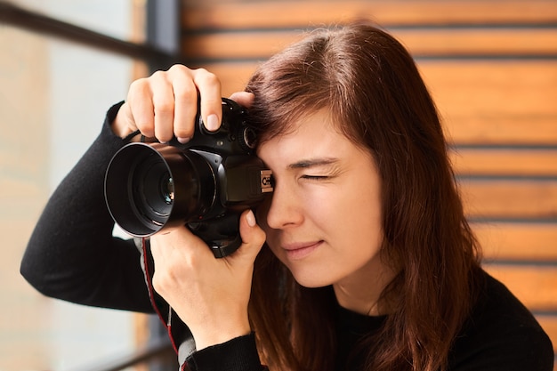 Fotograf der Frau, die Foto mit Kamera auf professionellem Fotoshooting mit Tageslicht nahe Fenster nimmt