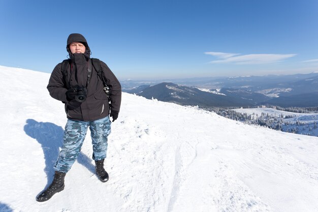 Fotograf, der mit Kamera auf Hügel mit Panoramablick des Wintertals steht