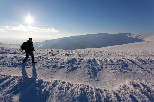 Fotograf des jungen Mannes in der Winterkleidung stehend und Foto mit Kamera im Sonnenlicht mit weißem Schneehintergrund machend