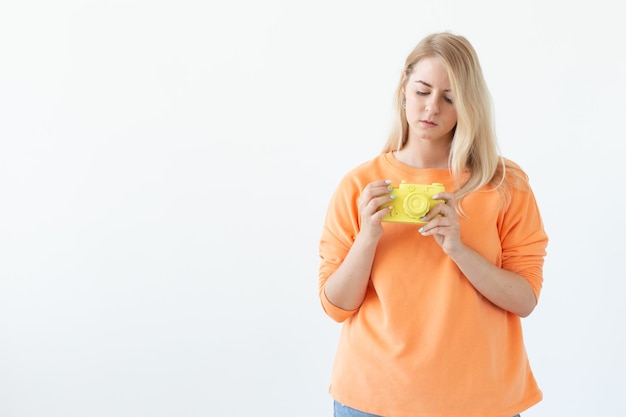 Fotograf, Hobby und Freizeitkonzept - Junge blonde Frau mit Retro-Kamera auf weißer Wand