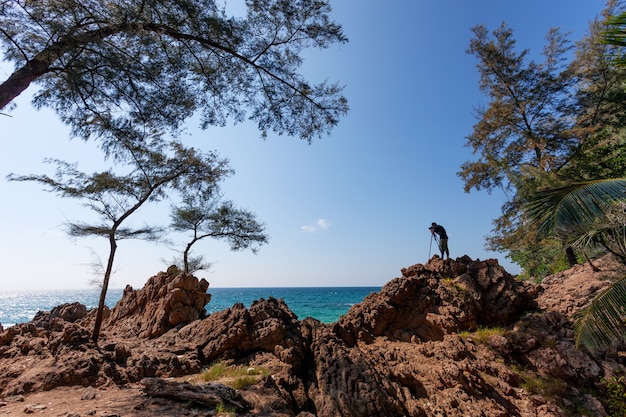 Foto fotograf mann, der auf felsenklippe steht, hat schießsession wilde seelandschaft.