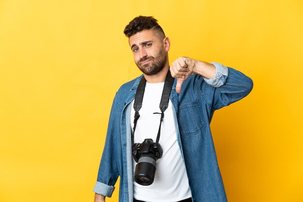 Fotograf Mann lokalisiert auf gelbem Hintergrund zeigt Daumen nach unten mit negativem Ausdruck