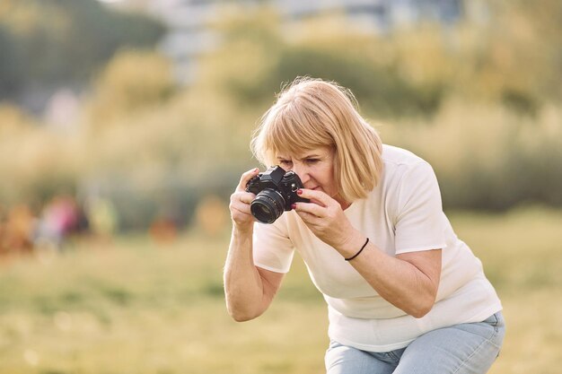 Foto fotograf mit einer kamera ältere frau, die an einem sonnigen tag ein schönes wochenende im freien auf dem feld hat