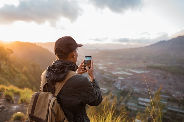 Fotograf mit Rucksack und Telefon, das Foto von Bergen macht