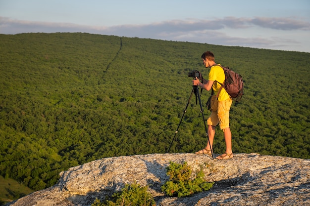 Fotograf mit Stativ und Rucksack am Abend auf dem Felsen.