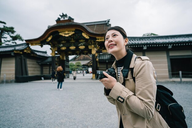 fotógrafa bonita tirando foto do templo com um grande sorriso no rosto. senhora viaja no Japão no inverno. visite o edifício tradicional japonês.