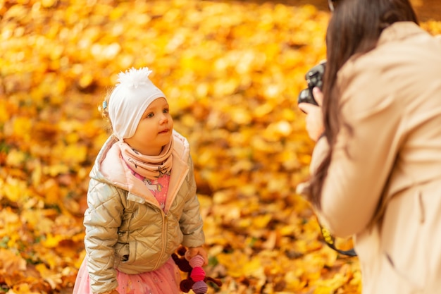 Fotógrafa e mãe tirando fotos da filha no parque de outono com folhagem amarela