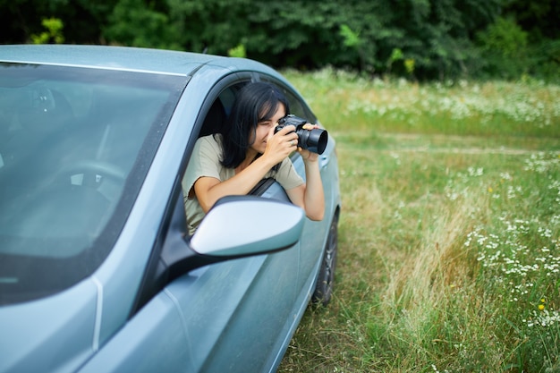 Fotógrafa sentada en el coche y fotografiando un paisaje de campo de flores, mujer de viaje toma una foto, espacio para texto.