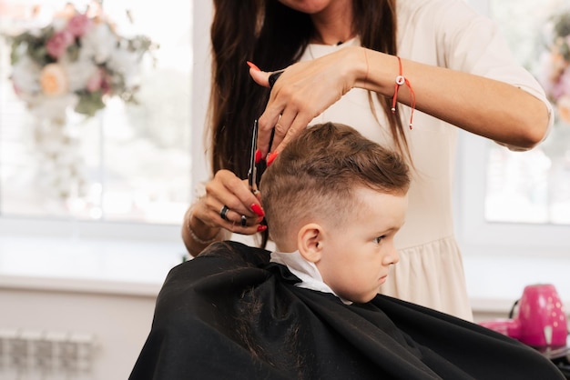 Fotografando em um salão de beleza Um barbeiro corta o cabelo de um garotinho com uma tesoura