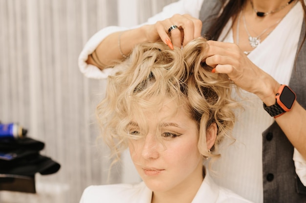 Fotografando em um salão de beleza Um cabeleireiro faz um penteado para uma jovem de cabelos escuros com a ajuda de um modelador de cabelo